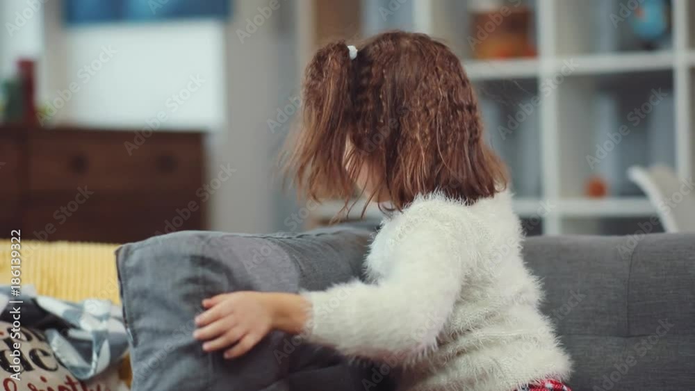 Cute little girl playing with pillow on the sofa in home child childhood happy room portrait close up apartment bedtime casual slow motion Cute little girl playing with pillow on the sofa in home child childhood happy room portrait close up apartment bedtime casual slow motion
