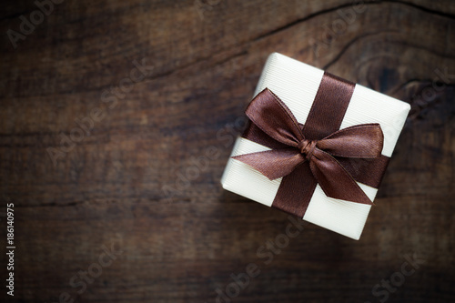 Beautiful gift box tied with a chocolate brown ribbon in a bow against dark rustic wooden background, Overhead view with plenty of copy space for your text