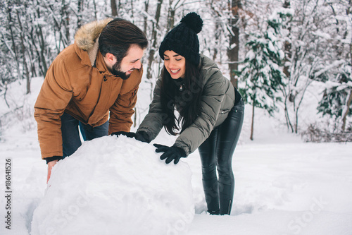 Happy Young Couple in Winter . Family Outdoors. man and woman looking upwards and laughing. Love, fun, season and people - walking in winter park. Making a snowman. photo