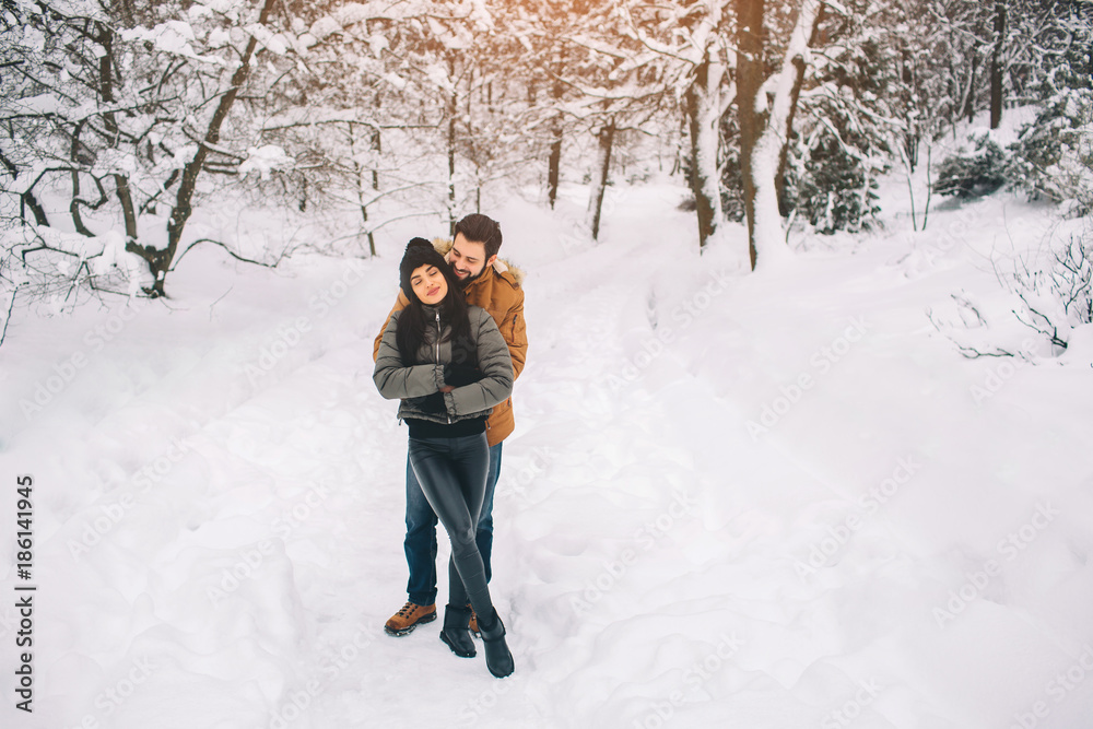 Happy Young Couple in Winter . Family Outdoors. man and woman looking upwards and laughing. Love, fun, season and people - walking in winter park. It's snowing, they're hugging