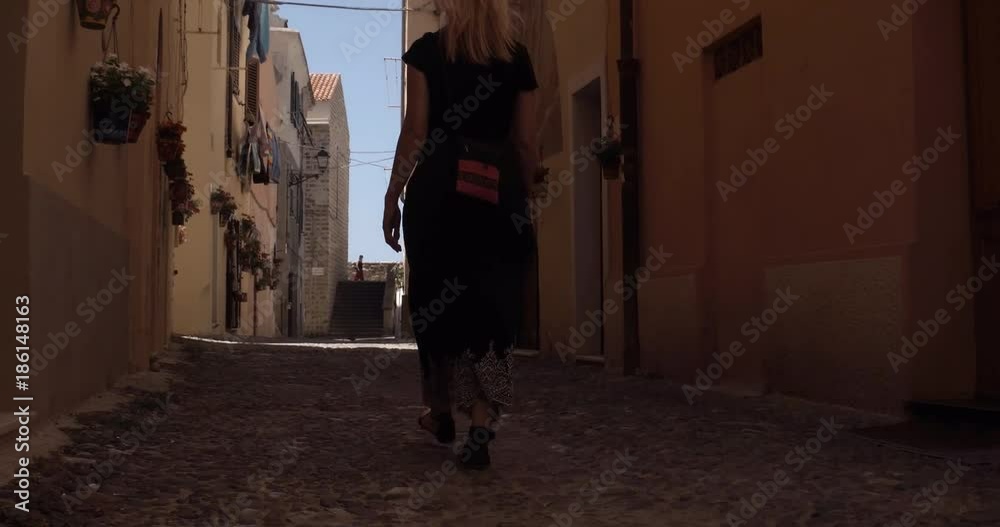 ALGHERO, SARDINIA, ITALY – JULY 2016 : Video shot of beautiful blonde girl walking in narrow street in central Alghero on a sunny day ALGHERO, SARDINIA, ITALY – JULY 2016 : Video shot of beautiful blonde girl walking in narrow street in central Alghero on a sunny day