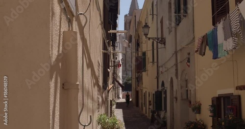 ALGHERO, SARDINIA, ITALY  – JULY 2016 : Video shot of beautiful blonde girl walking in narrow street in central Alghero on a sunny day
