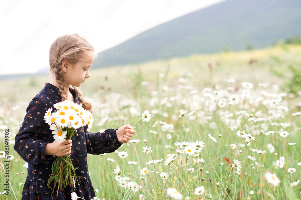Baby girl 3-4 year old picking up flowers in meadow. Holding camomiles outdoors. Spring season. Baby girl 3-4 year old picking up flowers in meadow. Holding camomiles outdoors. Spring season.