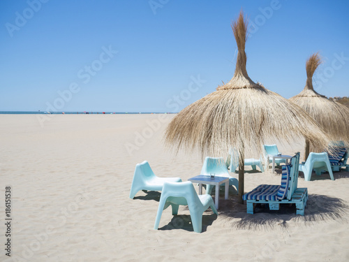 straw sunshades and blue chairs on a beach with golden sand in summer in andalucia, spain. Isla canela beach near ayamonte. photo