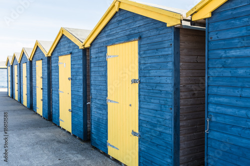 blue and yellow wooden beach huts in a row at Minnis Bay in Thanet kent, UK