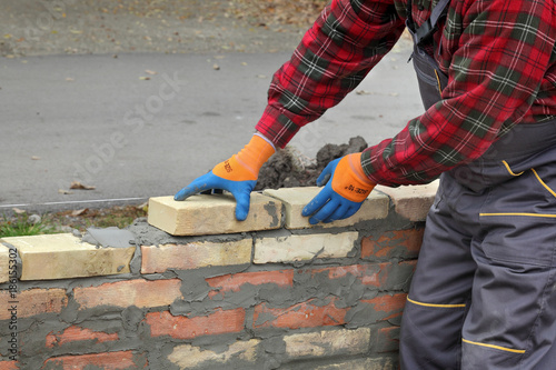 Mason worker making wall with mortar and bricks, closeup of hands placing brick
