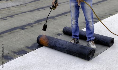 Roofer installing rolls of bituminous waterproofing membrane for the waterproofing of a terrace