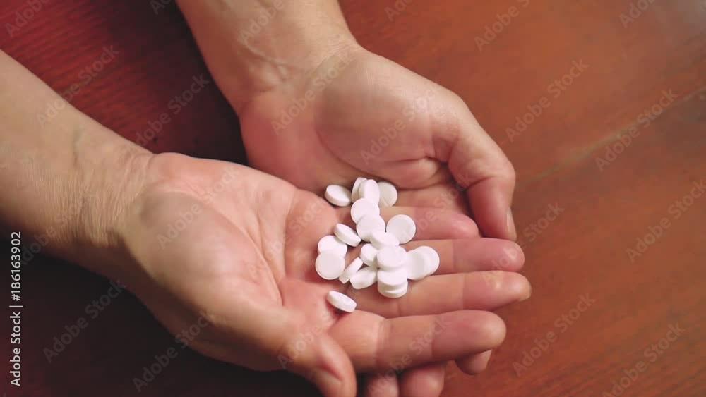 Handful of white tablets or pills in the hands of an elderly woman, copy space. Close-up shot of a hand holding white pills.