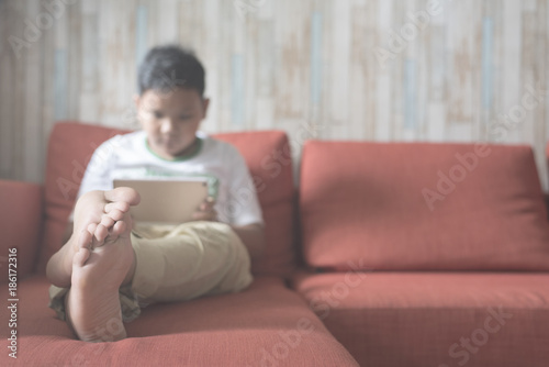 young asian boy using digital tablet on a sofa at home (focus on feet). boy relaxing on sofa at home. technology / IT concept. Computer learning concept .