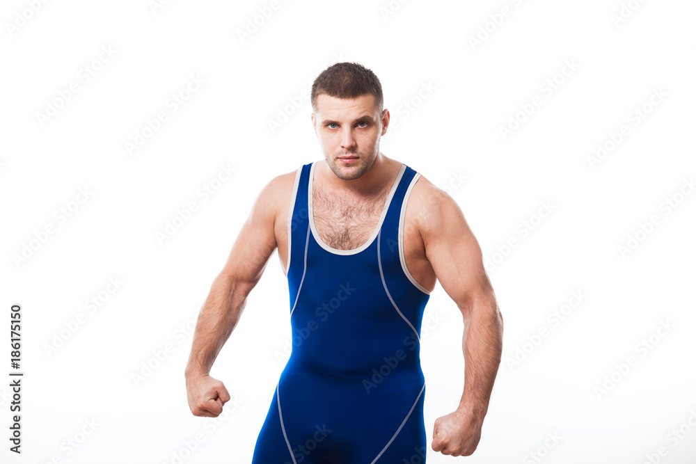 A young dark-haired man fighting wrestling, grappling in a blue wrestling tights smiles and holds his hands in fists in a fighting pose against a white isolated background A young dark-haired man fighting wrestling, grappling in a blue wrestling tights smiles and holds his hands in fists in a fighting pose against a white isolated background