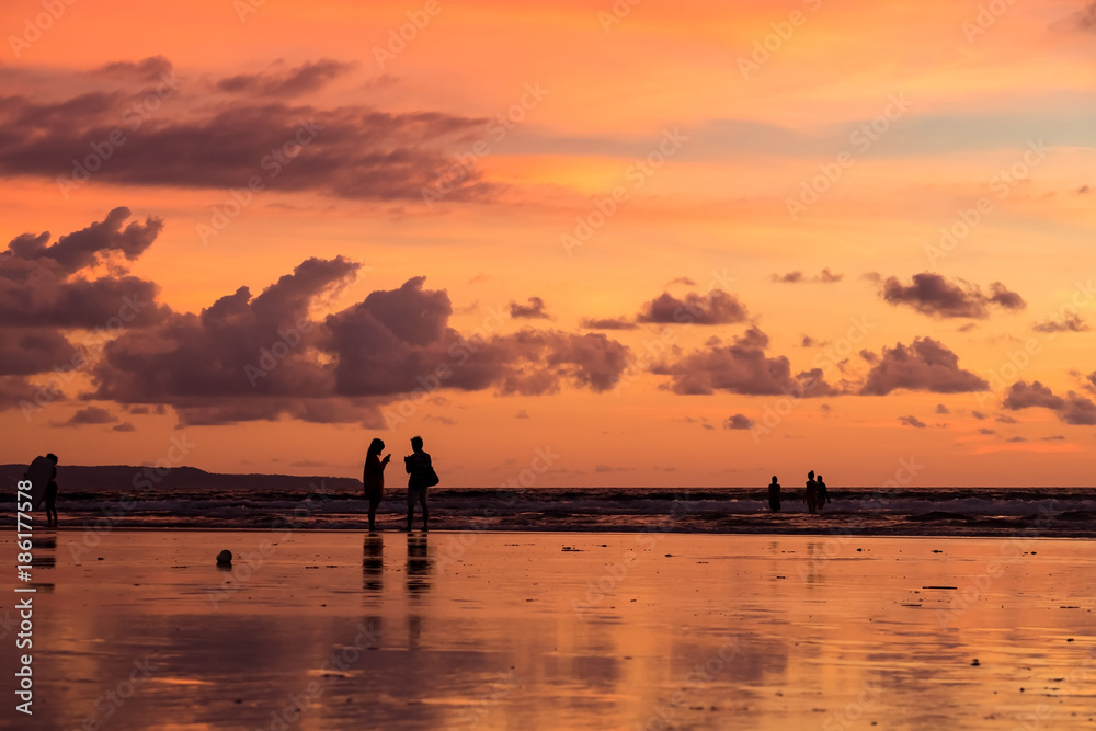 People silhouetted on the beach at sunset in Seminyak, Bali, Indonesia.