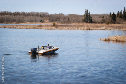 horizontal image of a man coasting along in his motorboat on a warm fall day.