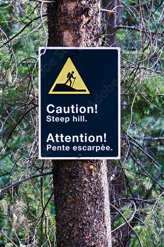 A caution steep hill sign on a edge of a trail