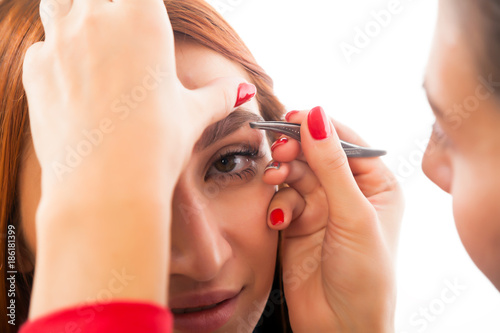 A woman's eyebrow plucked her eyebrows red-haired woman to achieve the ideal shape in a beauty salon, side view. Eyebrow correction procedures