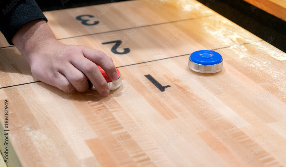 Vintage shuffle board game with red and blue disc and hand holding red