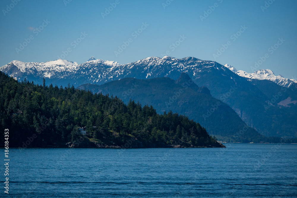 layered mountain range besides ocean under the blue sunny sky