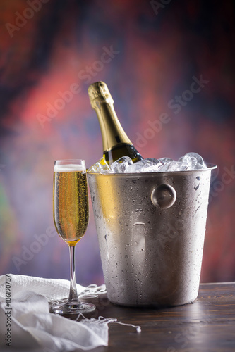 Champagne bottle in bucket with ice and glasses of champagne on dark background