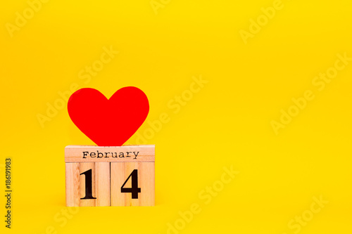 Happy Valentines Day card with red paper heart and wooden calendar on yellow background