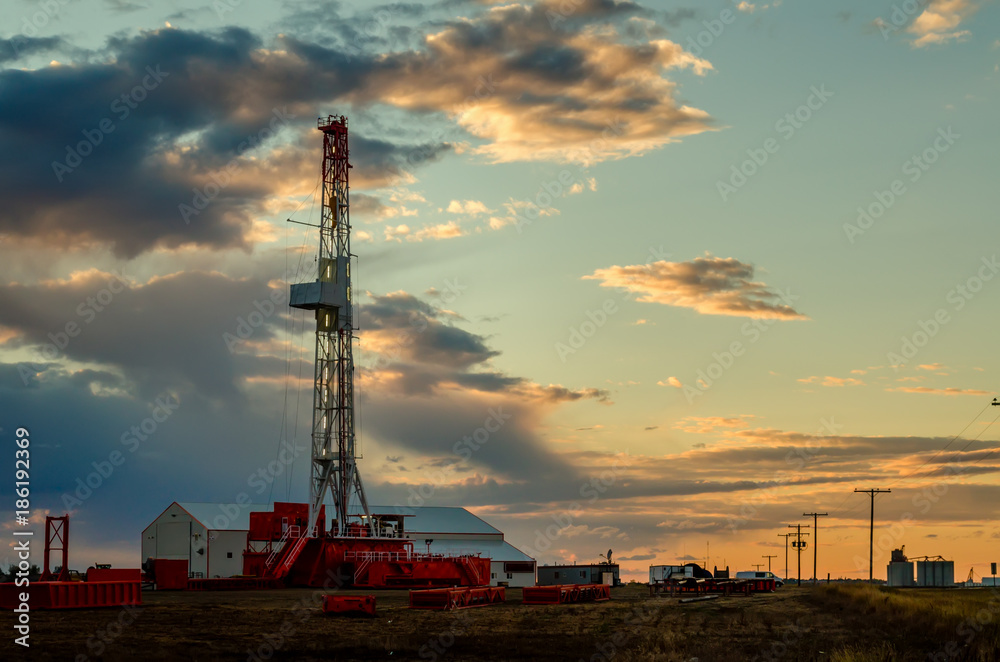Oil rig on the field at sunset with amazing cloudy sky, near the rail road in summer time