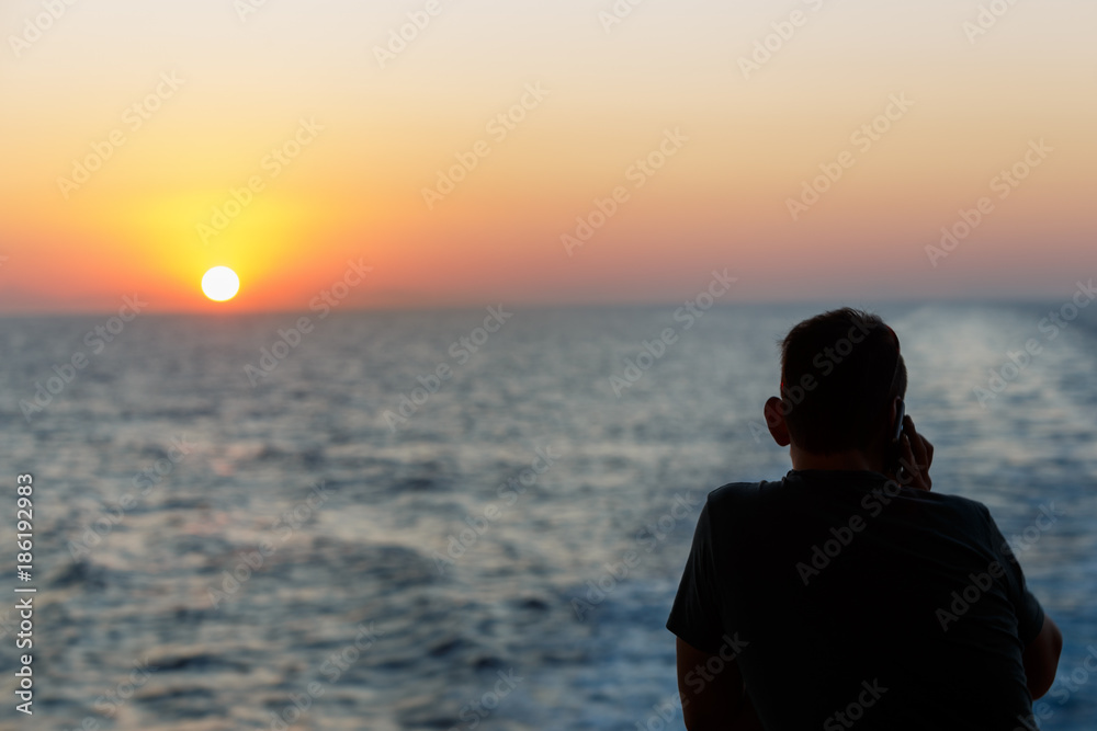 Silhouette of man standing alone on boat with blue sea and calling to someone at beautiful twilight sunset. Lonely man concept.