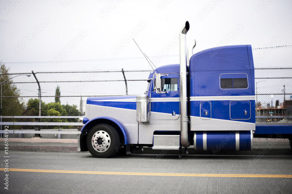 Blue powerful big rig semi truck tractor with chrome tall pipes on the road