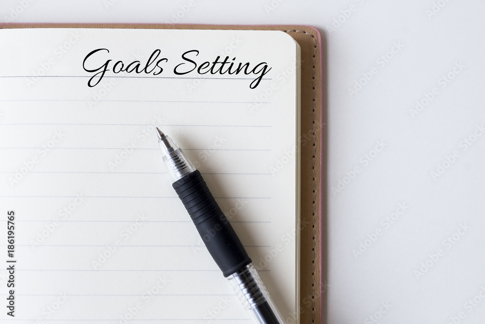 Conceptual,notebook on a white table. open diary and pen with goals setting words Conceptual,notebook on a white table. open diary and pen with goals setting words