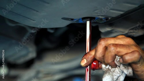 Auto Mechanic Draining Old Gear Oil Transaxle Underneath the Car Lift at the Garage