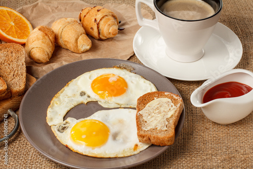 Wallpaper Mural Plate with fried eggs and toast with butter, croissants, bread on wooden cutting board, fresh orange, cup of black coffee and ketchup in a sauce boat Torontodigital.ca