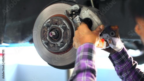 Auto Mechanic Repairing the Disc Brake Underneath the Car Lift at Garage