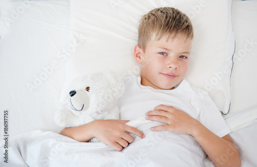 Little boy lying on the bed with toy bear. Space for text. Top view