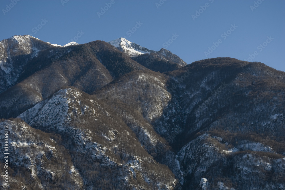 background: mountains, silhouette, beech and birch forests without leaves, covered with snow after a winter snowfall, sun and shadows, blue sky, sunset, winter, alps, Piedmont, Italy