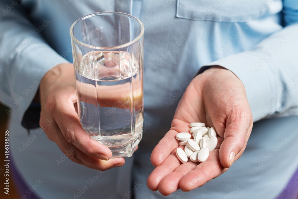 White medication pills, calcium dietary supplement in the woman palm hand and glass with water in the other hand - obrazy, fototapety, plakaty 