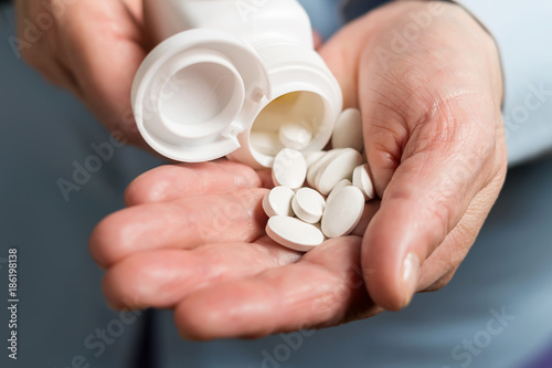 Woman hand holds white medication pills, pours from a white bottle into palm the calcium tablets dietary supplement