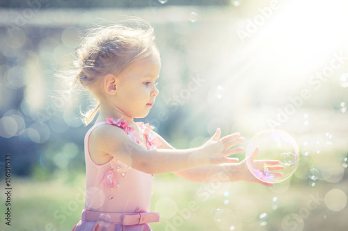 A little girl catches soap bubbles in summer park