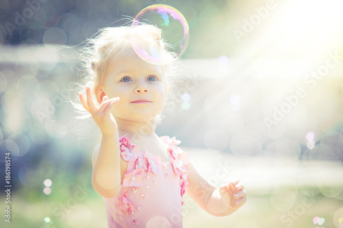 A little girl catches soap bubbles in summer park