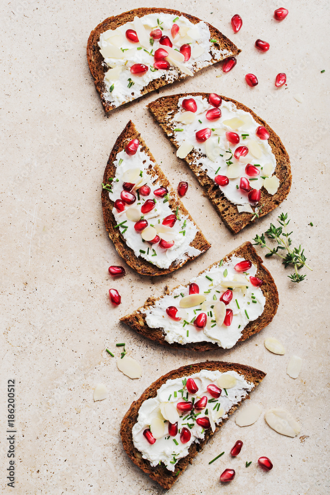 Open sandwiches rye bread with cream cheese and pomegranate seeds, flakes of almond on marble surface. Healthy snack concept. Top view. Open sandwiches rye bread with cream cheese and pomegranate seeds, flakes of almond on marble surface. Healthy snack concept. Top view.