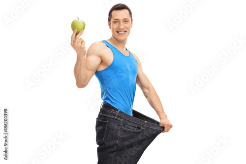 Guy in an oversized pair of jeans holding a green apple