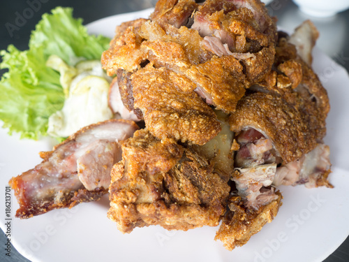 Crispy fried pork leg placed on a plate with vegetables and seasoning sauce
