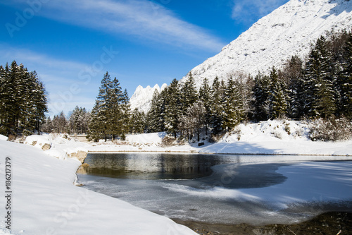 beautiful cold pure winter scenery on lake lago del predil in sunlight and blue sky, julina alps, Italy photo