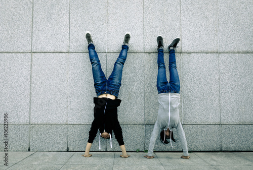 Obraz na plátně Two female hipster doing handstand against wall in city