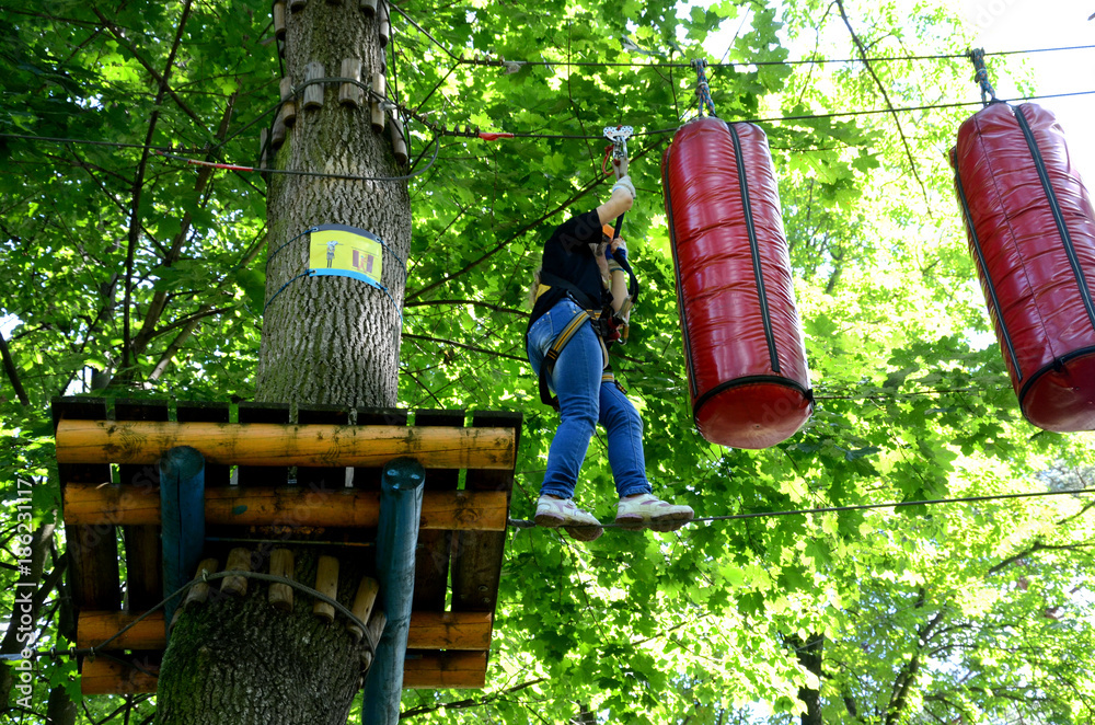 A child playing in a rope park on a background of trees