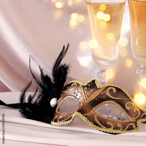 Image of elegant venetian mask and glasses of champagne over gold silk background.