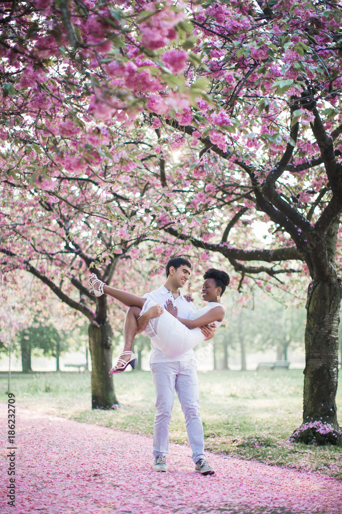 The young happy romantic couple walking by road with petals in the park and man holding woman in arms and they smiling The young happy romantic couple walking by road with petals in the park and man holding woman in arms and they smiling