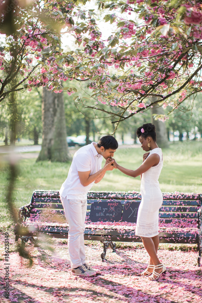 Fototapeta premium Side view of the young couple in love who standing in the park and man kissing woman's hand