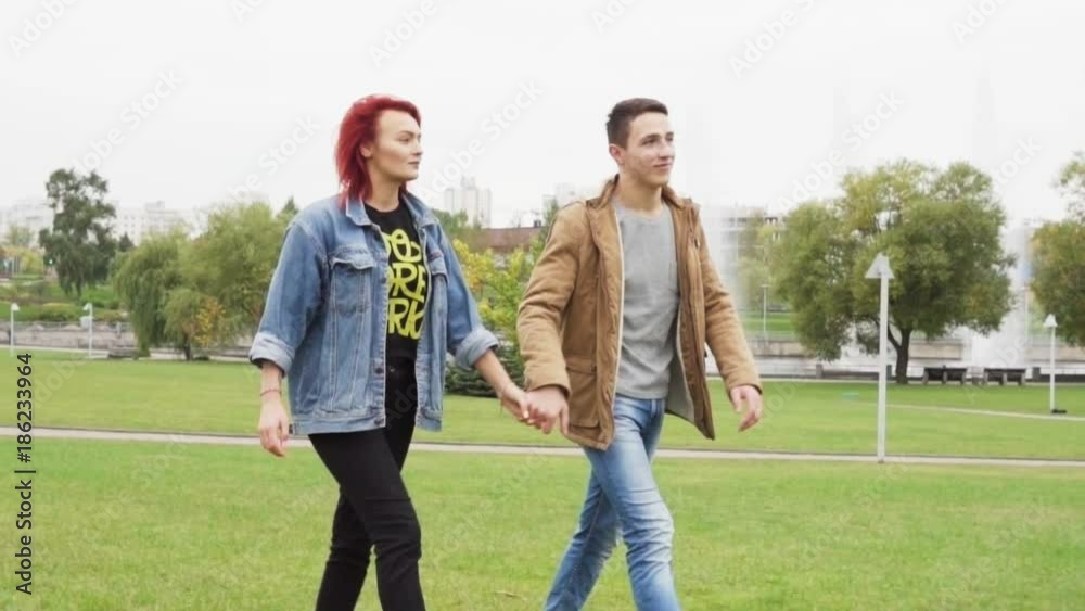 Young happy couple holding hands and walking in the city park, slow motion Young happy couple holding hands and walking in the city park, slow motion