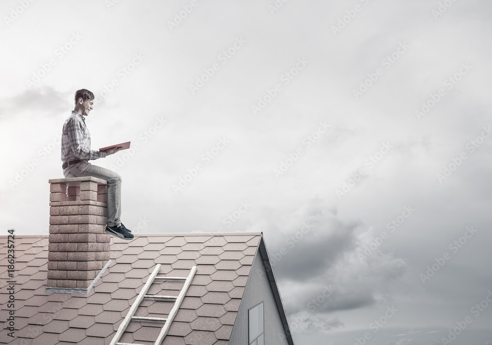 Handsome man on brick roof against cloud scape reading book Handsome man on brick roof against cloud scape reading book