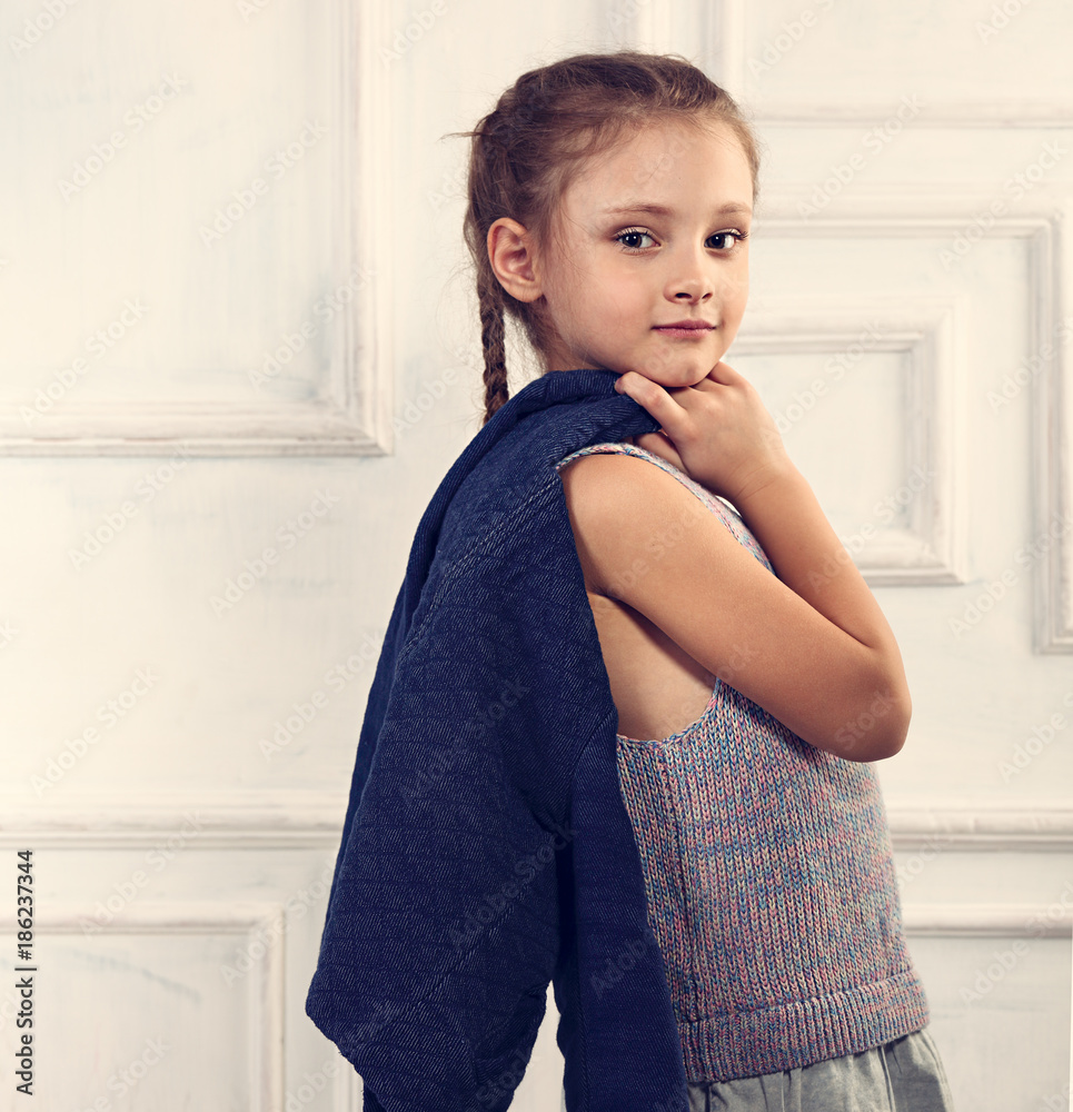 Smiling cute kid girl holding the blue jeans jacket on studio blue background. Closeup toned portrait Smiling cute kid girl holding the blue jeans jacket on studio blue background. Closeup toned portrait