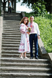 Lovely couple in ukrainian traditional embroidered clothing walk down the stairs with a bouquet.