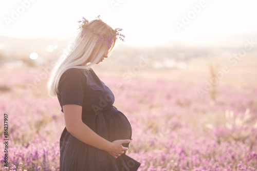 Pregnant blonde woman wearing dark blue dress in lavender field. Summer time. 20s.