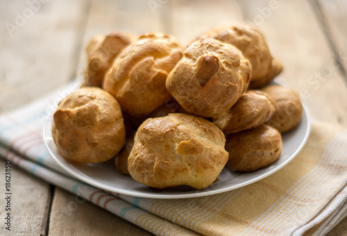 Isolated profiterole on a white plate on a dishcloth on a wooden table, 